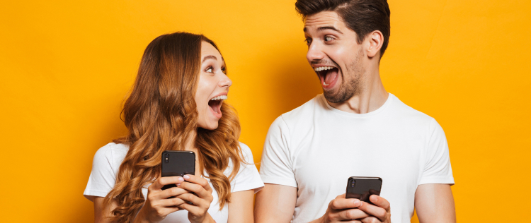 Šťastný mladý muž a žena sa na seba usmievajú, držia v rukách dva smartfóny.